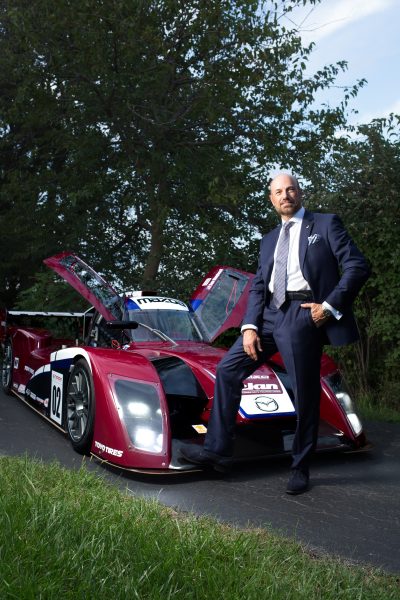 John Mangiameli standing in front of Mazda racer with right foot propped up on front